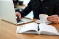 Male freelancer working on laptop in coffeehouse. Young man in black shirt drinks coffee to concentrate and cheer up. Cup of Royalty Free Stock Photo