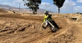 Male in a full-body riding suit is seen riding a dirt bike on a forest trail covered with mud