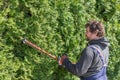 Male gardener in uniform using electric hedge cutter for work outdoors. Caucasian man shaping overgrown thuja during summer time Royalty Free Stock Photo