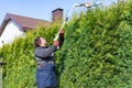 Male gardener using a long reach pole hedge trimmer to cut the top of a tall hedge. Professional gardener with a professional Royalty Free Stock Photo