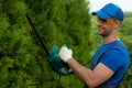 A male gardener wearing safety glasses cuts and shapes a thuja hedge with an electric trimmer Royalty Free Stock Photo