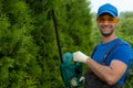 A male gardener wearing safety glasses cuts and shapes a thuja hedge with an electric trimmer Royalty Free Stock Photo