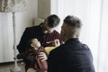 Male gay couple with adopted baby girl at home - Two handsome dads feed the baby girl on kitchen - Male babysitters - Lgbt family