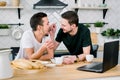 Male gay couple sitting at the table and having breakfast in their kitchen. Handsome young man in black t-shirt feeding Royalty Free Stock Photo