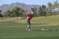 Male golfer hitting a golf ball from a back view.