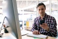 Male graphic designer using mobile phone while working on computer at desk in a modern office Royalty Free Stock Photo