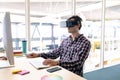Male graphic designer using virtual reality headset while working on computer at desk Royalty Free Stock Photo