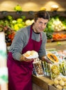 Male grocery store worker offers various packaged ripe fruits and vegetables