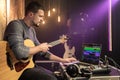 A male guitarist is recording a new song in a music studio using a special program on his laptop. Musical creativity concept