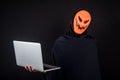 Male hacker with halloween mask carrying laptop