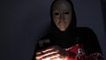 Male hacker hidden face with the mask accessing to personal information on laptop phone in the dark. Technology, cyber crime con