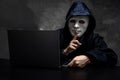 Male hacker hidden face with the mask and hoodie. Obscured dark face making silence gesture try to hack and steal information syst