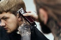 Male haircut with electric razor. Tattooed Barber makes haircut for client at the barber shop by using hairclipper. Man Royalty Free Stock Photo