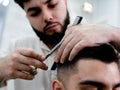 A dark-haired barber with a beard makes a fashionable haircut to a man in a barbershop using scissors and a comb Royalty Free Stock Photo