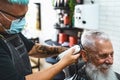 Male hairdresser cutting hair to hipster senior client while wearing face surgical mask - Young hairstylist working in barbershop