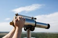 Male hand adjusts sharpness on a touristic binocular against forest panorama