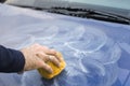 Male hand applies polishing paste on car paint with sponge