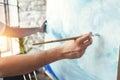 Male hand of artist closeup holding paintbrush on background of canvas on easel. Painter drawing ocean wave in loft studio. Flare Royalty Free Stock Photo