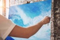 Male hand of artist closeup holding paintbrush on background of canvas on easel. Professional painter drawing ocean wave in loft s Royalty Free Stock Photo