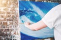 Male hand of artist holding paintbrush on background of canvas on easel. Professional painter drawing ocean wave in loft studio Royalty Free Stock Photo