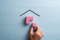 Male hand assembling a house made of pink wooden blocks over blue background Royalty Free Stock Photo