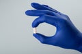 Male hand in a blue medical glove holding a white pill on a grey background. Royalty Free Stock Photo