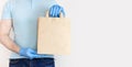 Male hand in blue medical gloves holds craft paper bag on white background. Delivery against Coronavirus 2019-nCov in pandemic