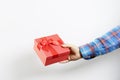 Male hand in a checkered sleeve holds a red holiday gift box with a bow on a white background Royalty Free Stock Photo