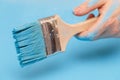 Male hand covered in paint, holding a paint brush on a wooden background surface, painted with blue paint