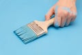 Male hand covered in paint, holding a paint brush on a wooden background surface