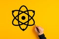 Male hand drawing an atom icon on yellow background. Science and technology