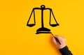 Male hand drawing a justice scale on yellow background. Fairness, equality or trust