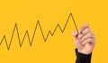 Male hand draws a fluctuating line graph on yellow background Royalty Free Stock Photo