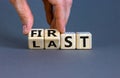 Male hand flips wooden cubes and changes the inscription `last` to `first` or vice versa. Beautiful grey background, copy spac Royalty Free Stock Photo