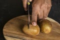 A male hand going to cut two ripe whole kiwi fruits on chopping board with knife on a black wooden surface. Selective focus Royalty Free Stock Photo