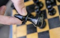 Male hand holding a black bishop chess piece above the board with figures