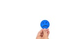 Male hand holding a blue sad face icon in white background with copy space. Sadness and loneliness concept. Royalty Free Stock Photo