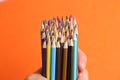 Male hand holding a bunch of colorful pencils on orange background Royalty Free Stock Photo