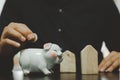 Male hand holding a coin in a white pig piggy bank. Business concepts, finance, savings, taxes and retirement investments