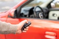 Male hand holding electronic remote key pushing button near red rental car