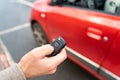 Male hand holding electronic remote key pushing button near red rental car