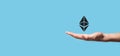 Male hand holding a Ethereum icon on blue background. Ethereum and cryptocurrency investing concept. exchanging, trading, transfer