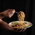 Male hand holding fork with large portion of spaghetti on black background. Serving food plate of pasta with salad Royalty Free Stock Photo