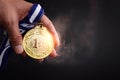 Male hand holding golden medal over dark background and light burst Royalty Free Stock Photo