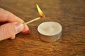 Male hand holding an ignited safety match stick before igniting white candle