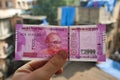 Male hand holding Indian two thousand rupee banknote with Mahatma Gandhi market blurred background