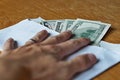 Male hand holding its fingers on white envelope full of American Dollars (USD, US Dollars) on the wooden table as a symbol of Royalty Free Stock Photo