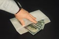 Male hand holding its fingers on white envelope full of American Dollars Royalty Free Stock Photo