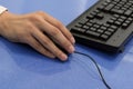 Male hand is holding a mouse next to the keyboard. Close-up. An office worker or manager works on a computer. Blue background Royalty Free Stock Photo