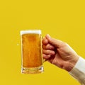 Male hand holding mug of cold, foamy lager, golden beer against vivid yellow studio background. Oktoberfest. Royalty Free Stock Photo